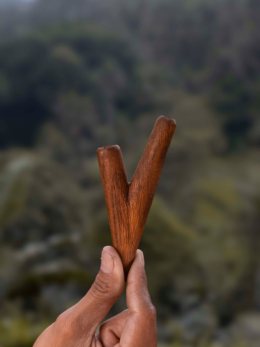 Hand holding a wooden tool against a blurred natural background