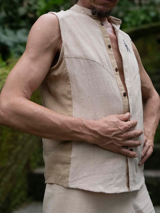 Man wearing a beige sleeveless vest over a shirt with a blurred natural background