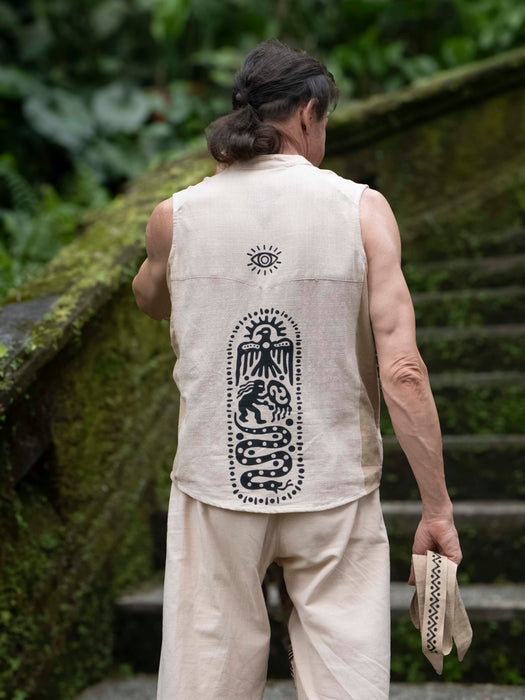 Person wearing a sleeveless beige shirt with a black design, standing outdoors.