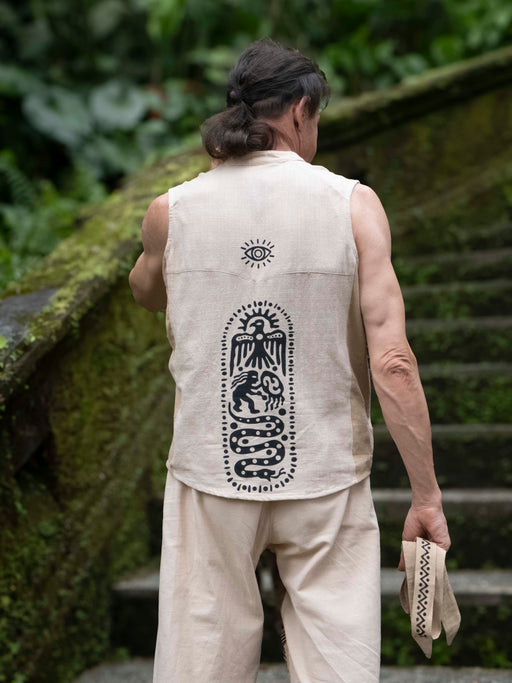 Person wearing a sleeveless beige shirt with a black design, standing outdoors.