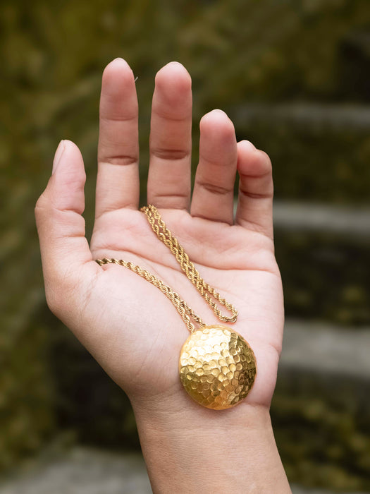 Gold necklace with a round pendant held in a hand against a blurred natural background