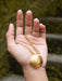 Gold necklace with a round pendant held in a hand against a blurred natural background
