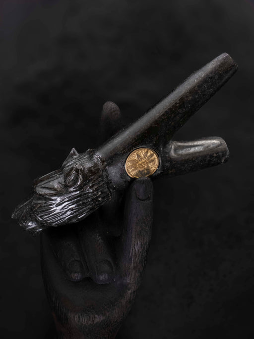 Decorative object with wolf head design held by a gloved hand against a dark background