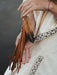 Powerful eagle feather bound with red thread and turquoise stones, hanging against a weathered leather pouch for ceremonial use.