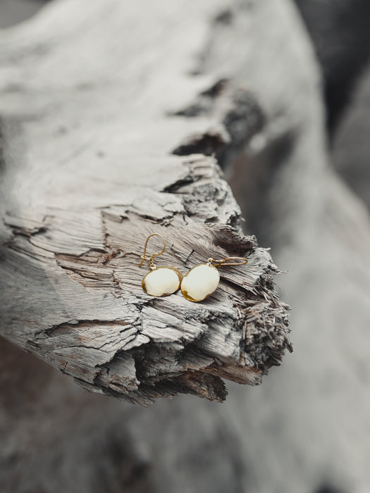 Hand-engraved bronze earrings featuring sacred geometry patterns, hanging against a rustic leather pouch