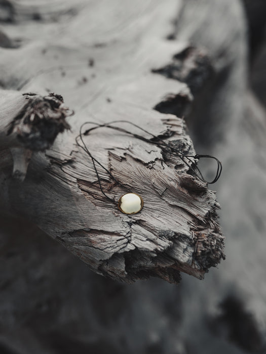 Copper pendant with a polished mirror disc, hanging from a leather cord against a backdrop of dried sage and feathers