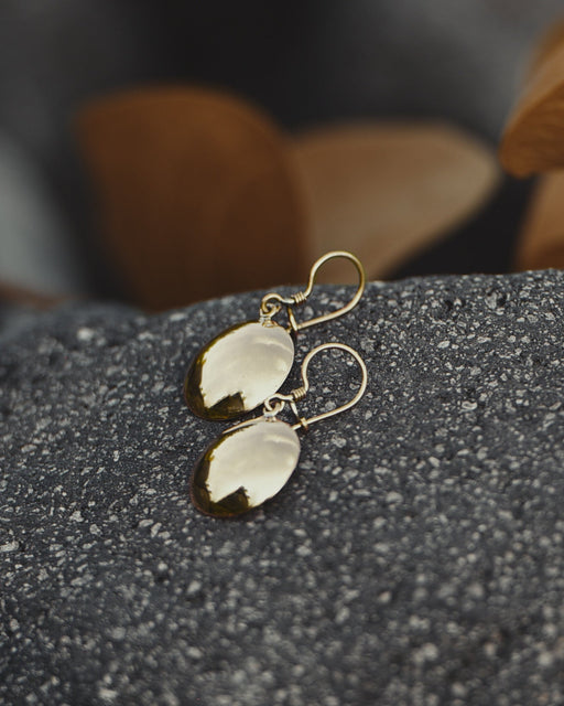 Close-up of artisan-crafted bronze earrings with circular mirrors, showcasing intricate tribal engravings on textured metal