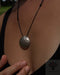 Necklace with a textured pendant worn by a person, brand 'AYAHO' visible.