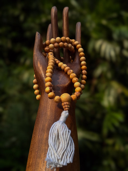 Wooden mala beads with a tassel on a wooden stand against a blurred green background