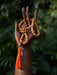 Wooden hand holding a string of beads with an orange tassel against a blurred green background