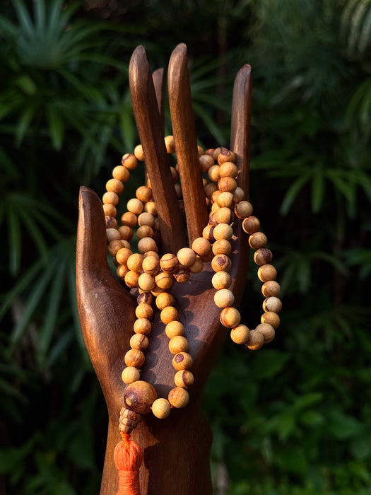 Wooden salad servers with a wooden bead necklace against a green leafy background