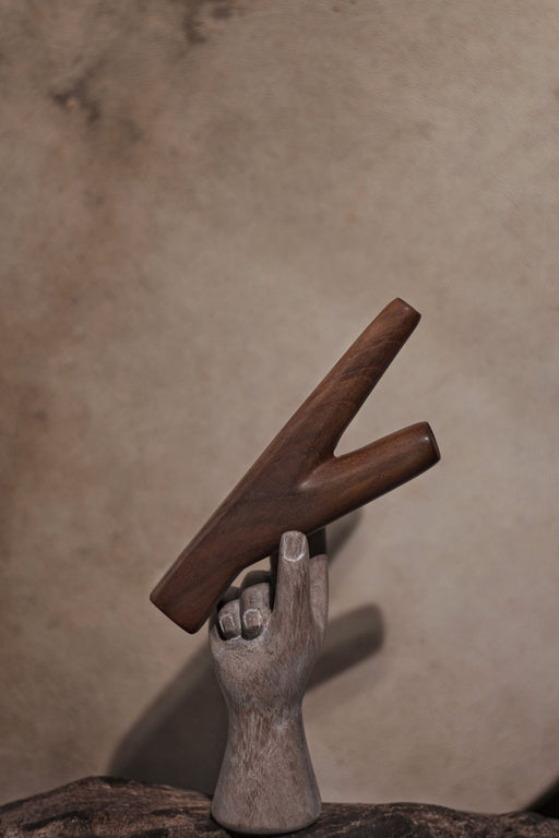 Wooden letter 'K' held by a stone hand against a beige background