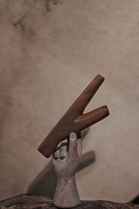 Wooden letter 'K' held by a stone hand against a beige background