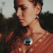 Woman wearing a necklace and earrings with a blurred natural background