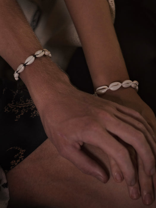 Close-up of hands wearing shell bracelets on a dark background