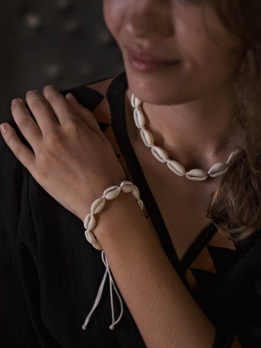 Close-up of a person wearing a shell bracelet and necklace against a dark background
