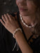 Close-up of a person wearing a shell bracelet and necklace against a dark background