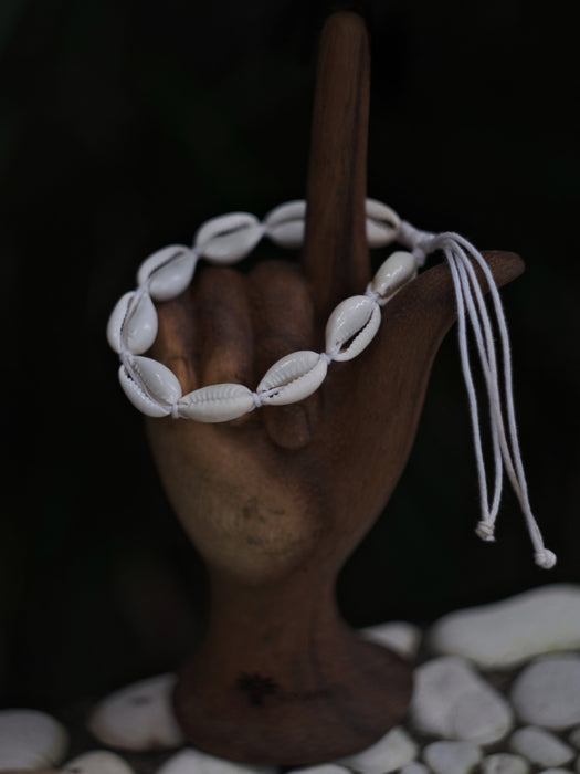 Bracelet made of cowrie shells on a wooden hand with a dark background