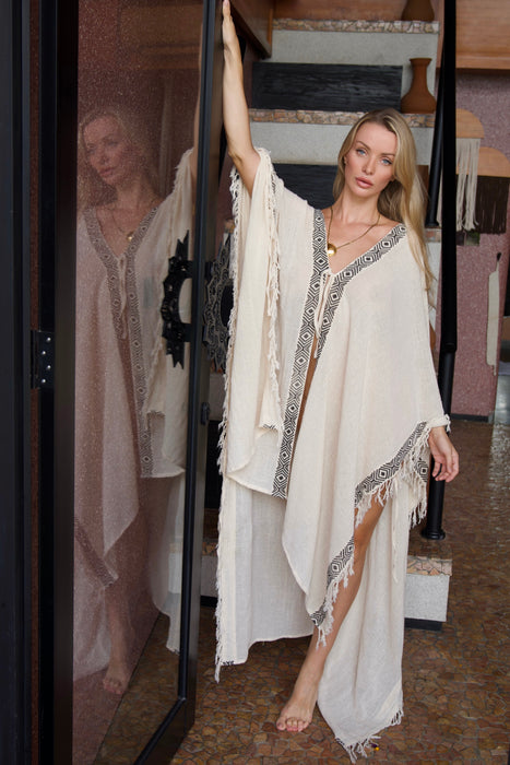 Woman in a white dress with fringe standing in front of a mirror.