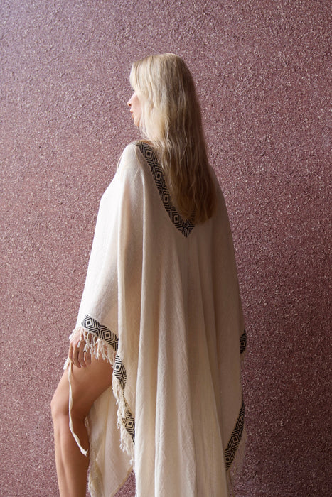 Woman wearing a white cape with decorative trim against a textured pink wall