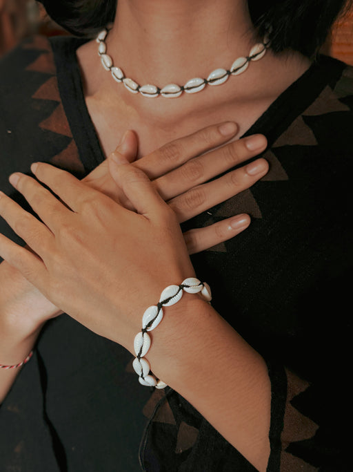 Person wearing a shell bracelet and necklace on a dark background