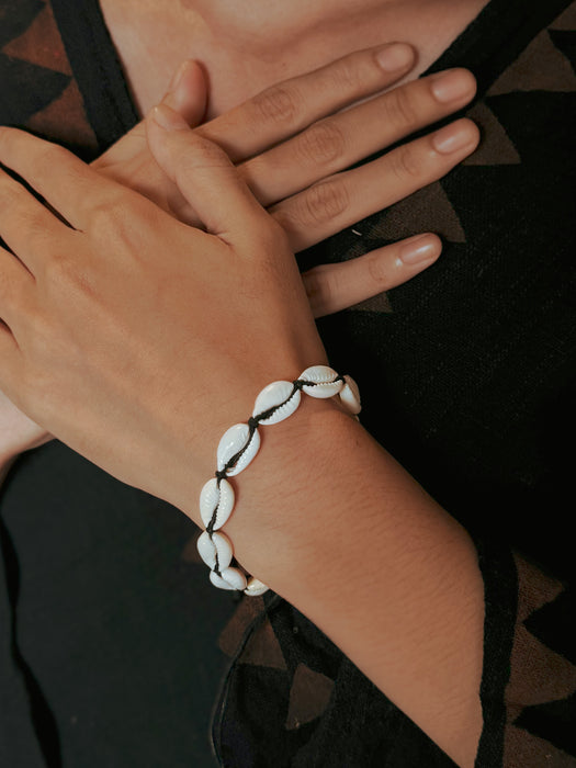 Close-up of a hand wearing a white beaded bracelet on a dark background