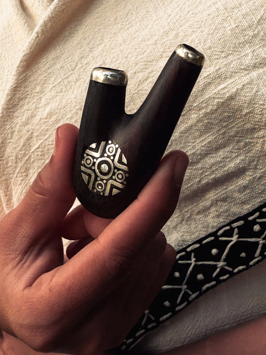Hand holding a black and silver decorative object against a light fabric background