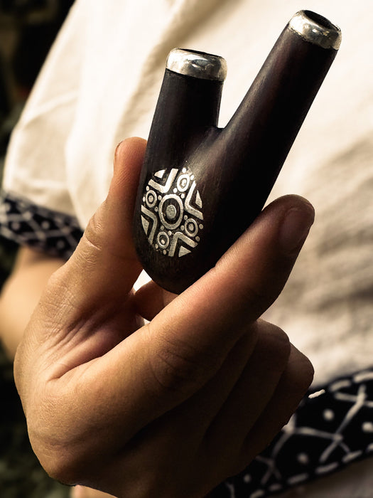 Hand holding a black and silver object with intricate design, against a blurred background.