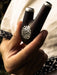 Hand holding a black and silver object with intricate design, against a blurred background.