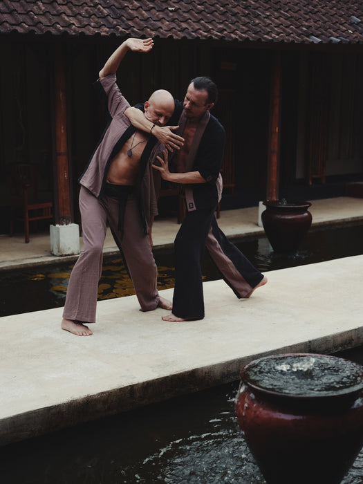 Two men practicing martial arts by a pool with traditional architecture in the background