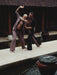 Two men practicing martial arts by a pool with traditional architecture in the background