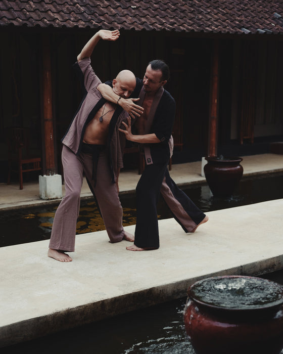 Two men practicing martial arts by a pool with traditional architecture in the background