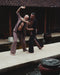 Two men practicing martial arts by a pool with traditional architecture in the background