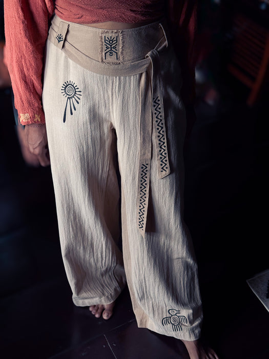 Light-colored pants with tribal designs worn by a person, against a dark background