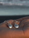 Silver earrings on a hand with a blurred ocean background