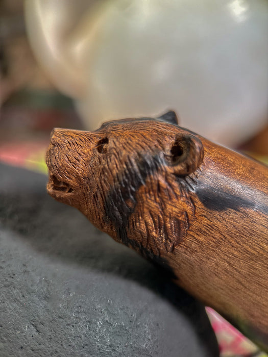 Wooden handle with a carved bear face design on a blurred background