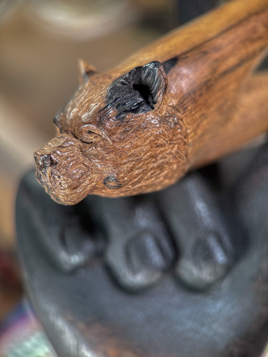 Wooden handle with a carved animal head design held by a dark-colored hand.