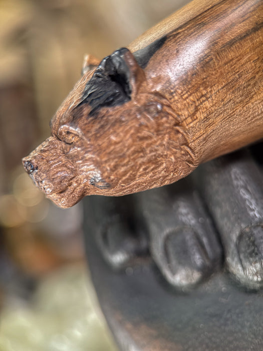 Close-up of a wooden handle with a carved animal head design, blurred background