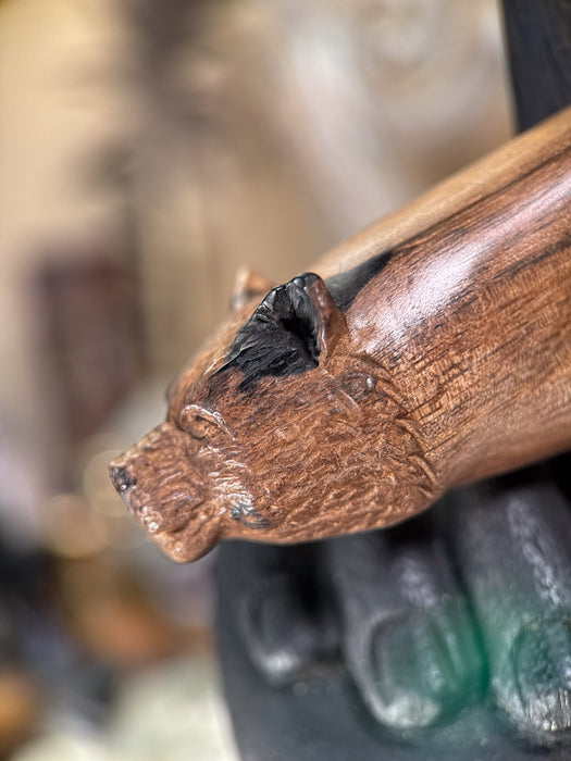 Wooden handle with a carved bear head design, held by a person's hand.