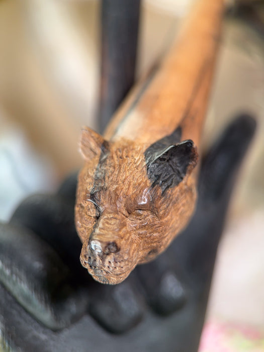 Close-up of a small wooden sculpture held by a gloved hand against a blurred background
