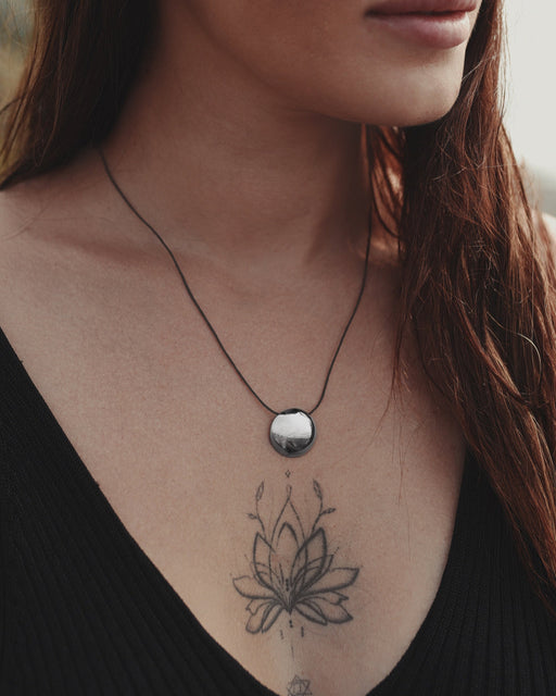 Close-up of a woman's neck with a necklace and a tattoo of a lotus flower on her chest.