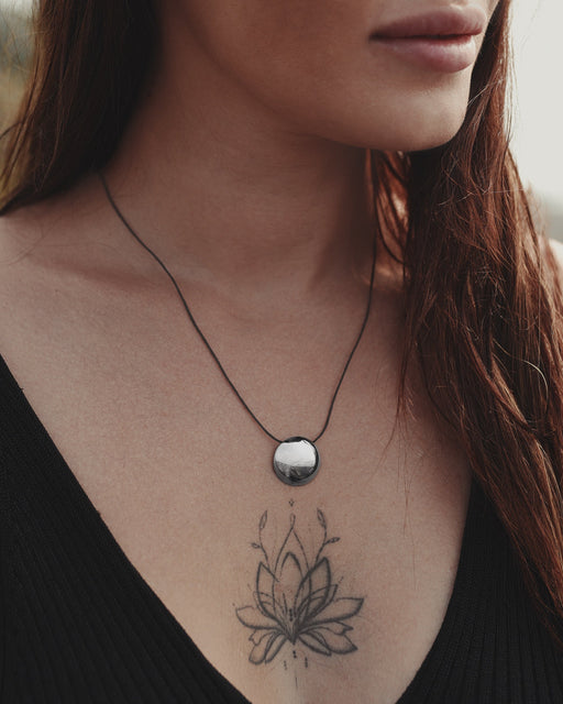 Close-up of a woman's neck with a necklace and a tattoo of a lotus flower on her chest.