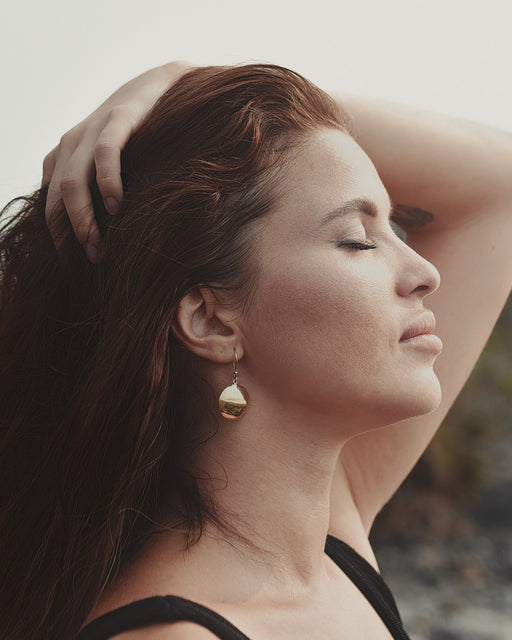 Bronze earrings with symbolic engravings and reflective mirrors, placed beside sage and crystals.