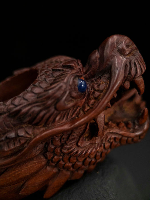Carved wooden dragon head with a blue stone in its mouth on a dark background