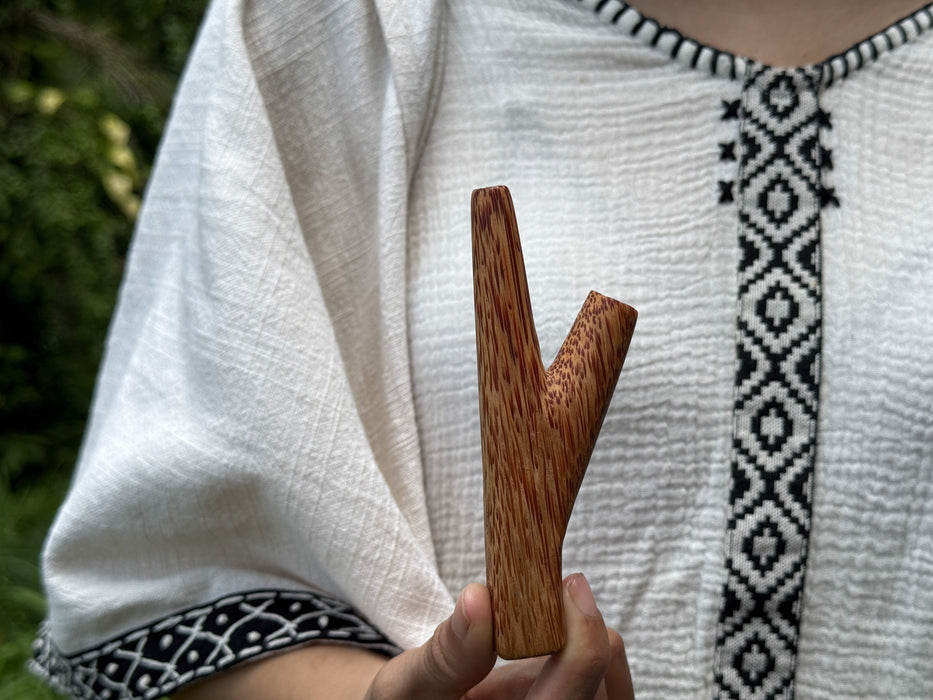 Person holding a wooden tool against a white garment with black patterns.
