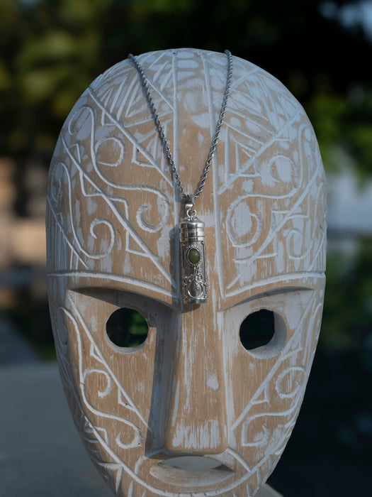 Carved wooden mask with intricate patterns and a necklace with a pendant on a blurred natural background