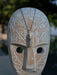 Carved wooden mask with intricate patterns and a necklace with a pendant on a blurred natural background