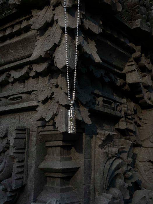 Silver pendant necklace hanging against a dark, textured background