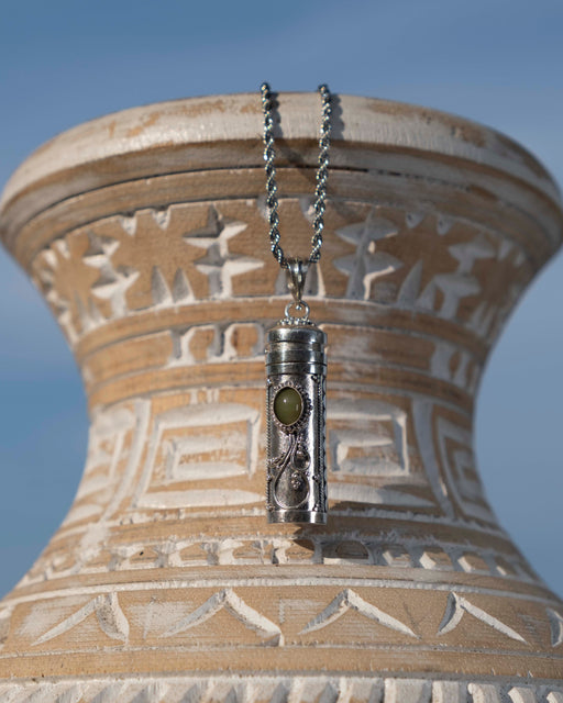 Silver pendant with a green stone on a chain against an ornate beige vase.