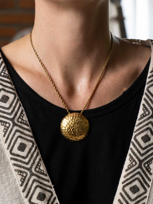 Gold necklace with a large round pendant worn by a person.